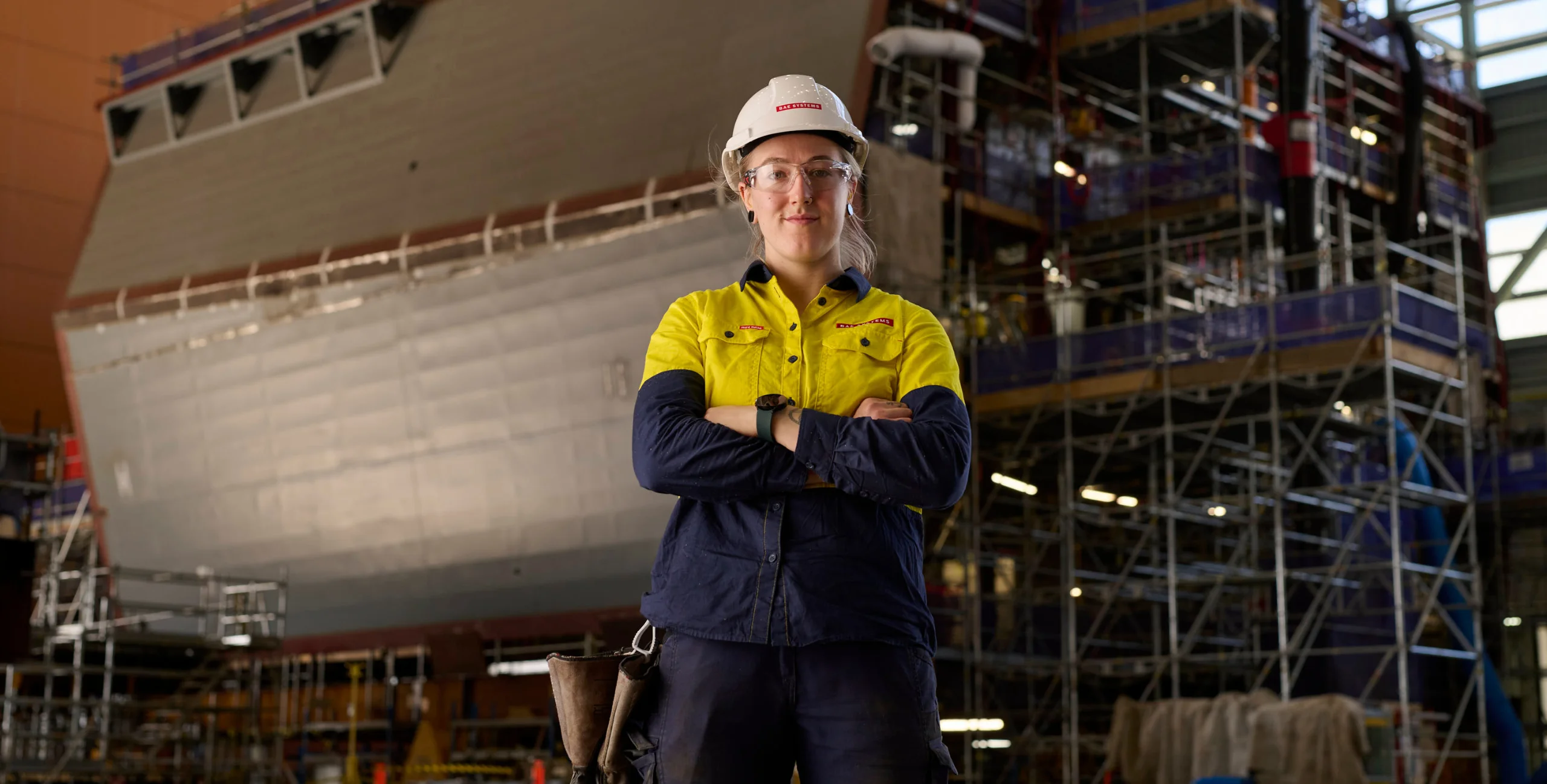 BAE Systems Welder standing proudly in front of an incomplete hull in a shipyard