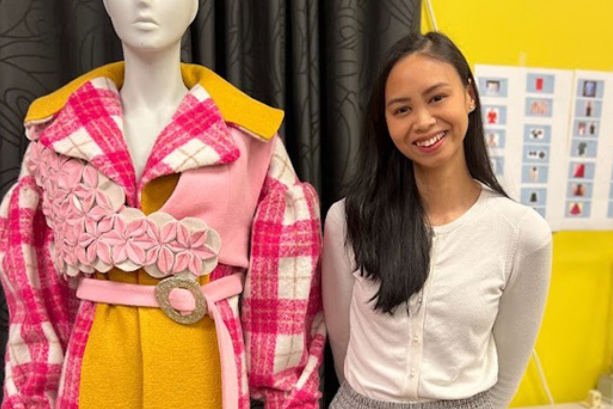 Aurelie Sowerbutts stands beside a mannequin dressed in a colorful outfit with pink plaid patterns and yellow accents.