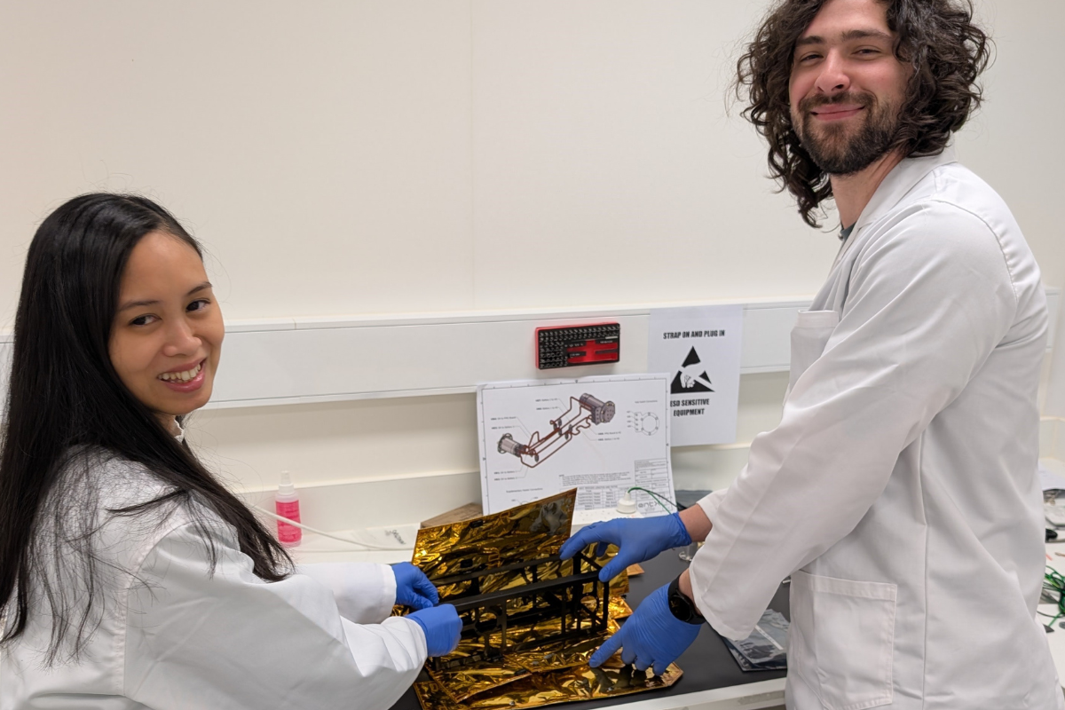 Aurelie Sowerbutts and Allan Dias in white coats and blue gloves work on a project involving gold foil in a lab.