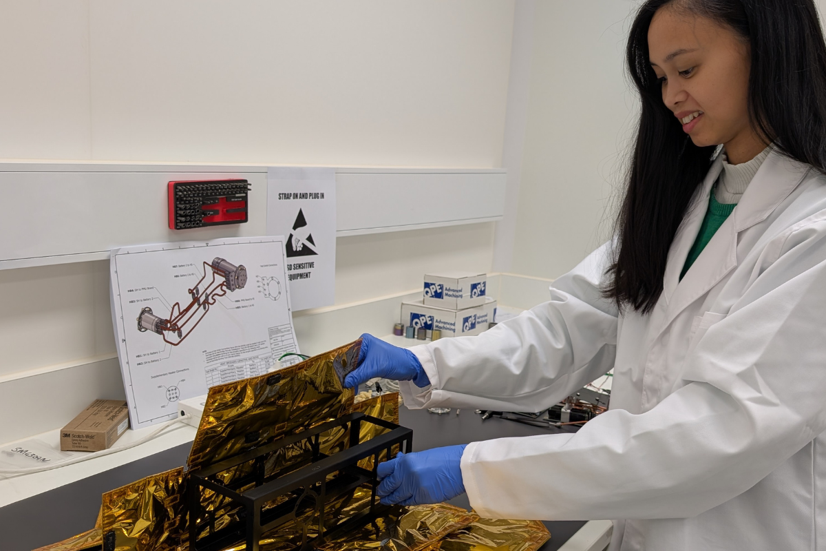 Aurelie Sowerbutts in a lab coat and gloves inspects a gold-foil-covered object in a lab. 
